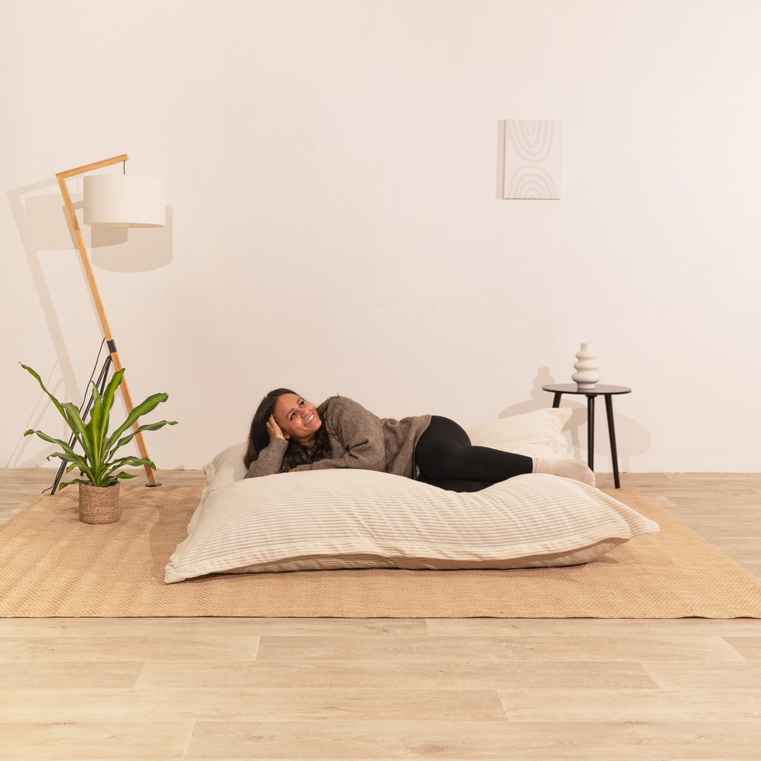 Personne assise sur un pouf 140x180 cm blanc cassé en velours côtelé, dans un décor d&