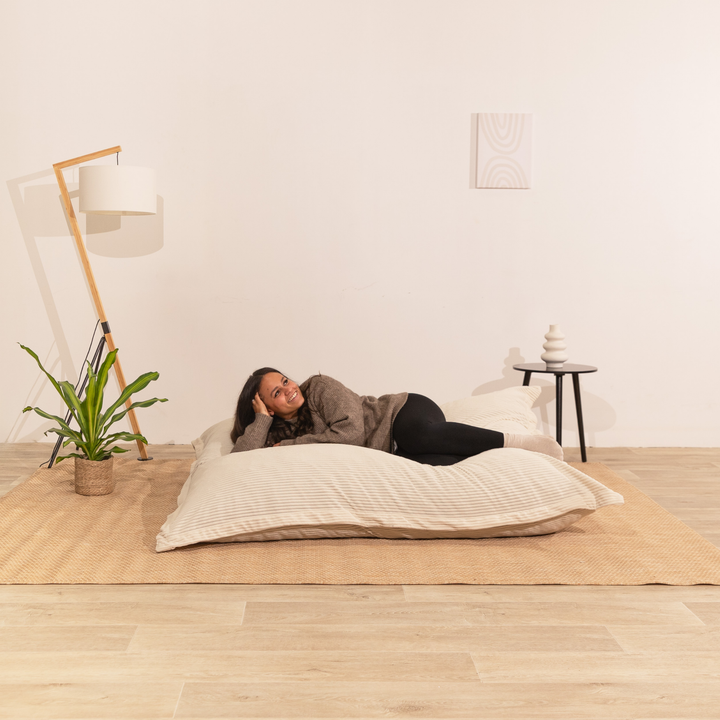 Personne assise sur un pouf 140x180 cm blanc cassé en velours côtelé, dans un décor d&
