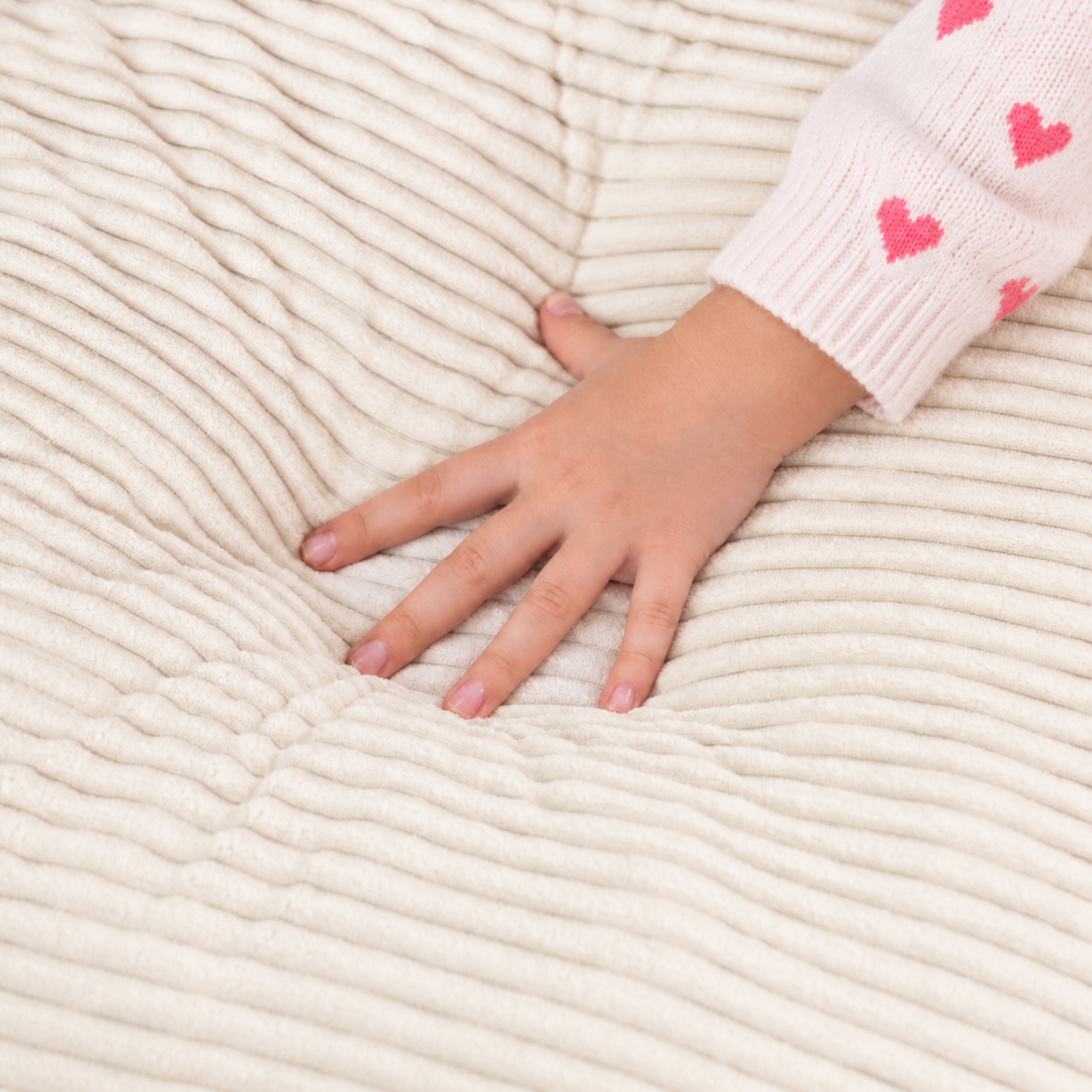 Pouf fauteuil enfant en velours côtelé blanc cassé, main d’enfant posée sur le tissu de l&