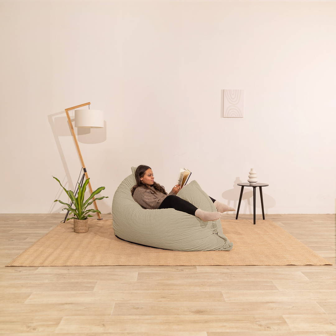 Personne assise sur un pouf 140x180 cm beige en velours côtelé, dans un décor d&