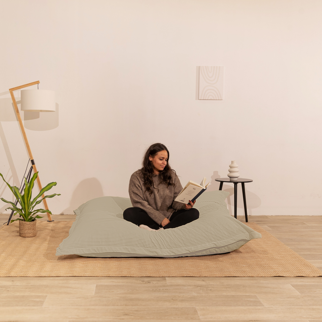 Personne assise sur un pouf 140x180 cm beige en velours côtelé, dans un décor d&