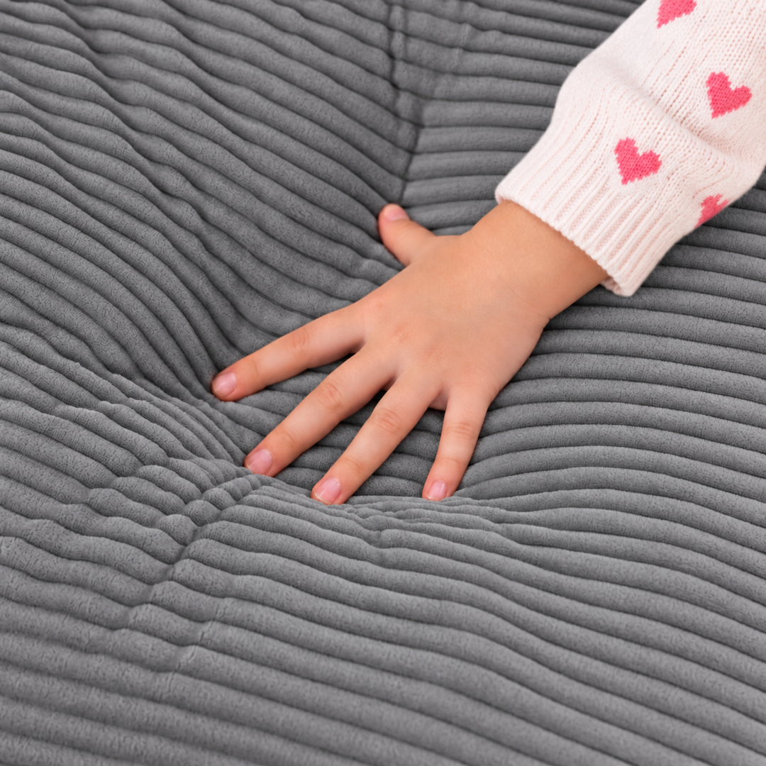 Fauteuil pouf enfant en velours côtelé gris foncé, main posée sur l’assise côtelée