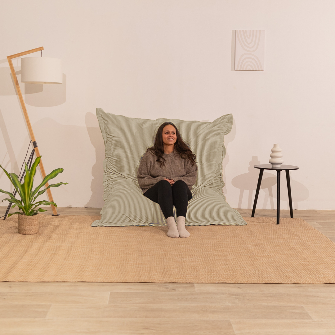 Personne assise sur un pouf 140x180 cm beige en velours côtelé, dossier appuyé contre le mur dans un décor d&