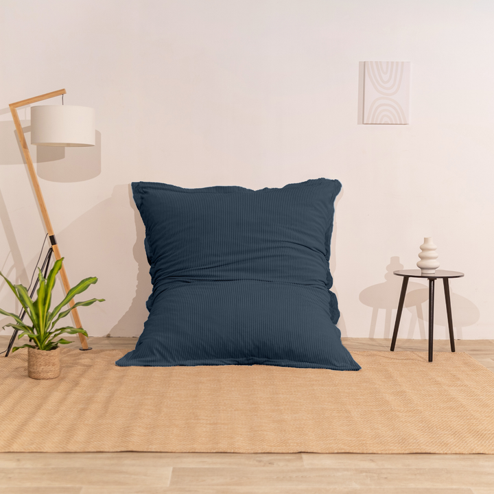 Pouf 140x180 bleu nuit en velours côtelé déhoussable, appuyé contre un mur dans un décor d&