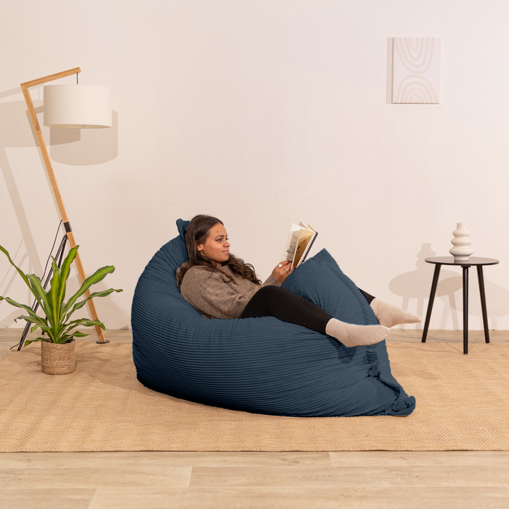 Personne assise sur un pouf 140x180 cm bleu nuit en velours côtelé, dans un décor d&