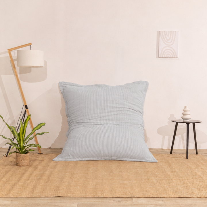 Pouf 140x180 gris clair en velours côtelé déhoussable, appuyé contre un mur.