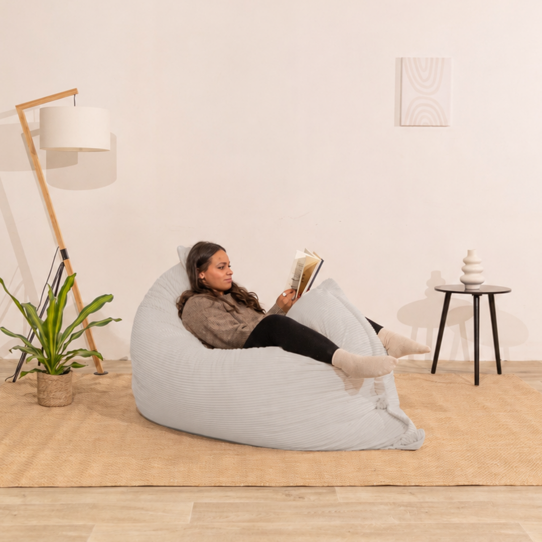 Personne assise sur un pouf 140x180 cm gris clair en velours côtelé, dans un décor d&