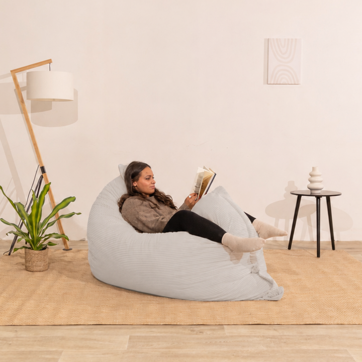 Personne assise sur un pouf 140x180 cm gris clair en velours côtelé, dans un décor d&