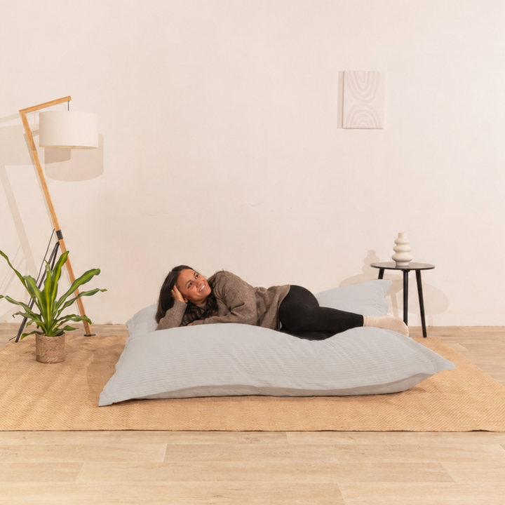 Personne allongée sur un pouf 140x180 cm gris clair en velours côtelé, dans un décor d&