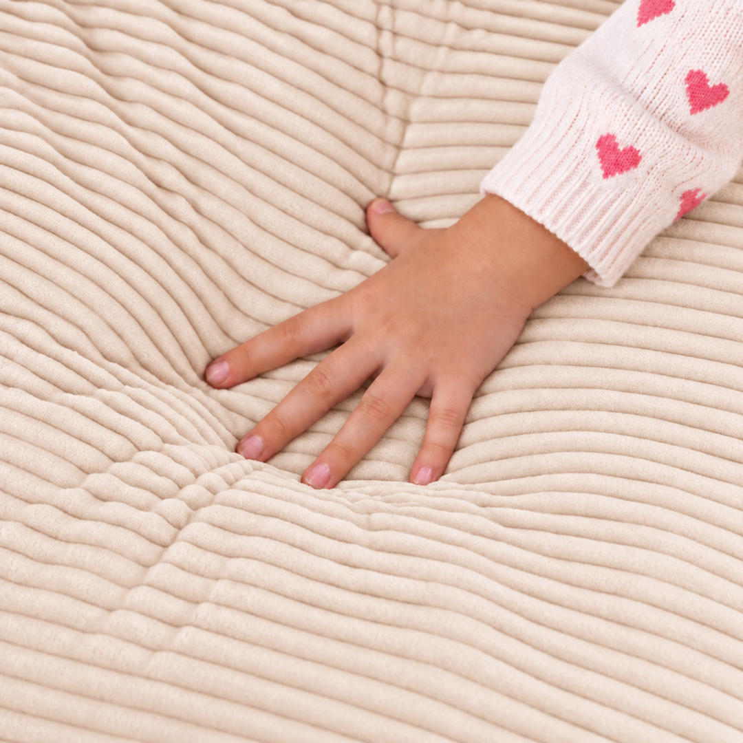 Fauteuil-pouf enfant en velours côtelé beige, main sur l’assise côtelée
