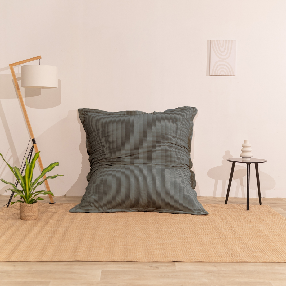 Pouf 140x180 gris foncé en velours côtelé déhoussable, appuyé contre un mur dans un décor d&