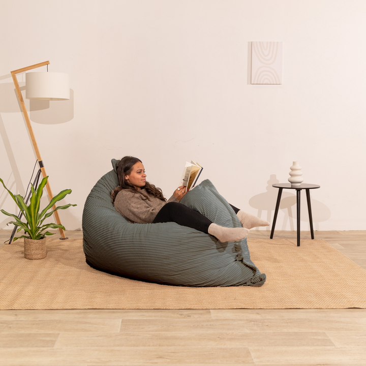 Personne assise sur un pouf 140x180 cm gris foncé en velours côtelé, dans un décor d&