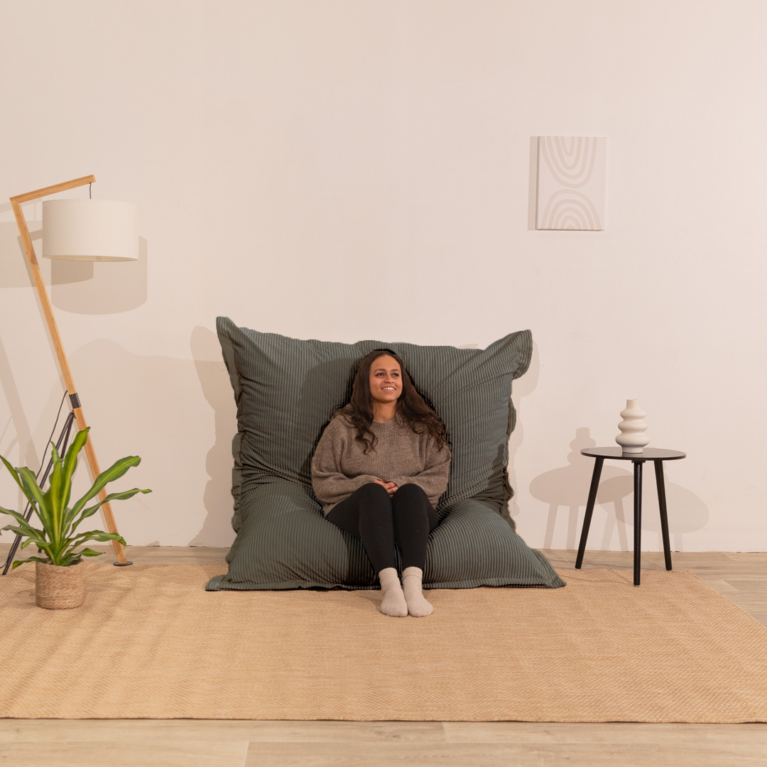 Personne assise sur un pouf 140x180 cm en velours côtelé, dossier appuyé contre le mur dans un décor d&