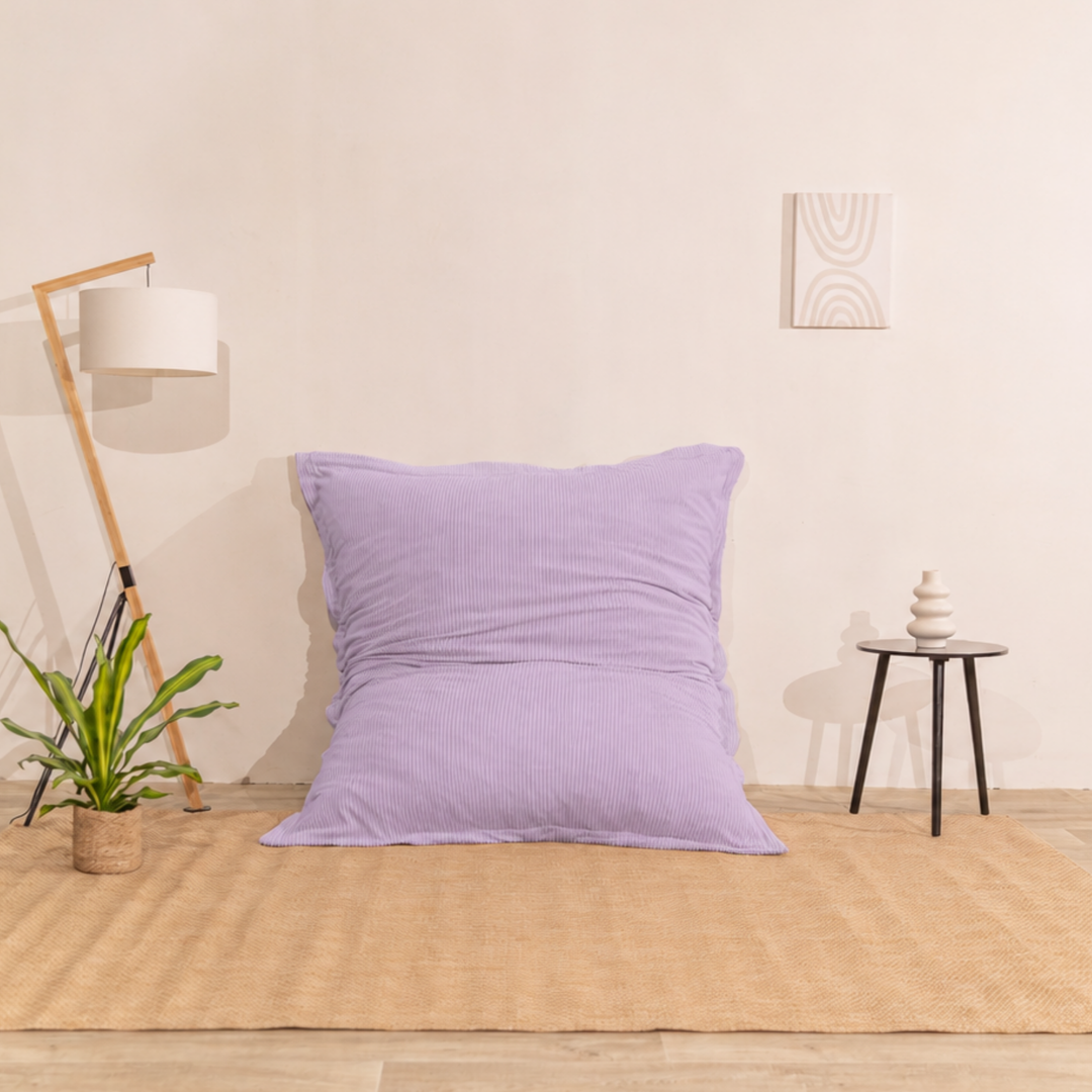 Pouf 140x180 violet en velours côtelé déhoussable, appuyé contre un mur.