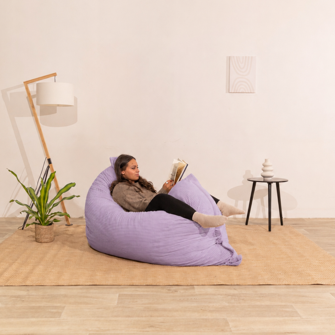 Personne assise sur un pouf 140x180 cm violet en velours côtelé, dans un décor d&