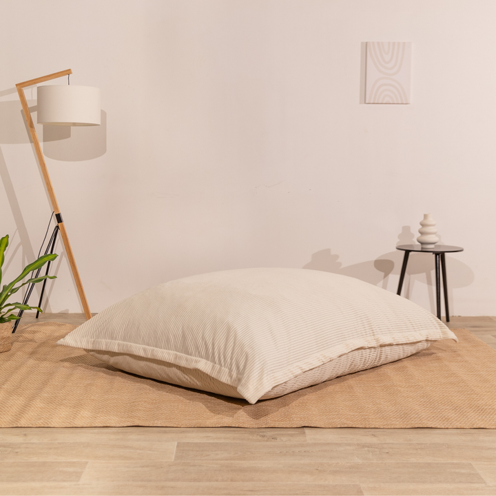 Pouf déhoussable velours côtelé blanc cassé, posé à plat dans un décor d&