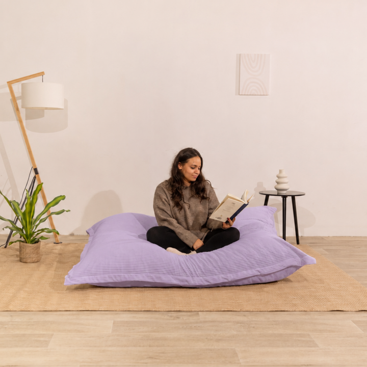 Personne assise sur un pouf 140x180 cm violet en velours côtelé, dans un décor d&