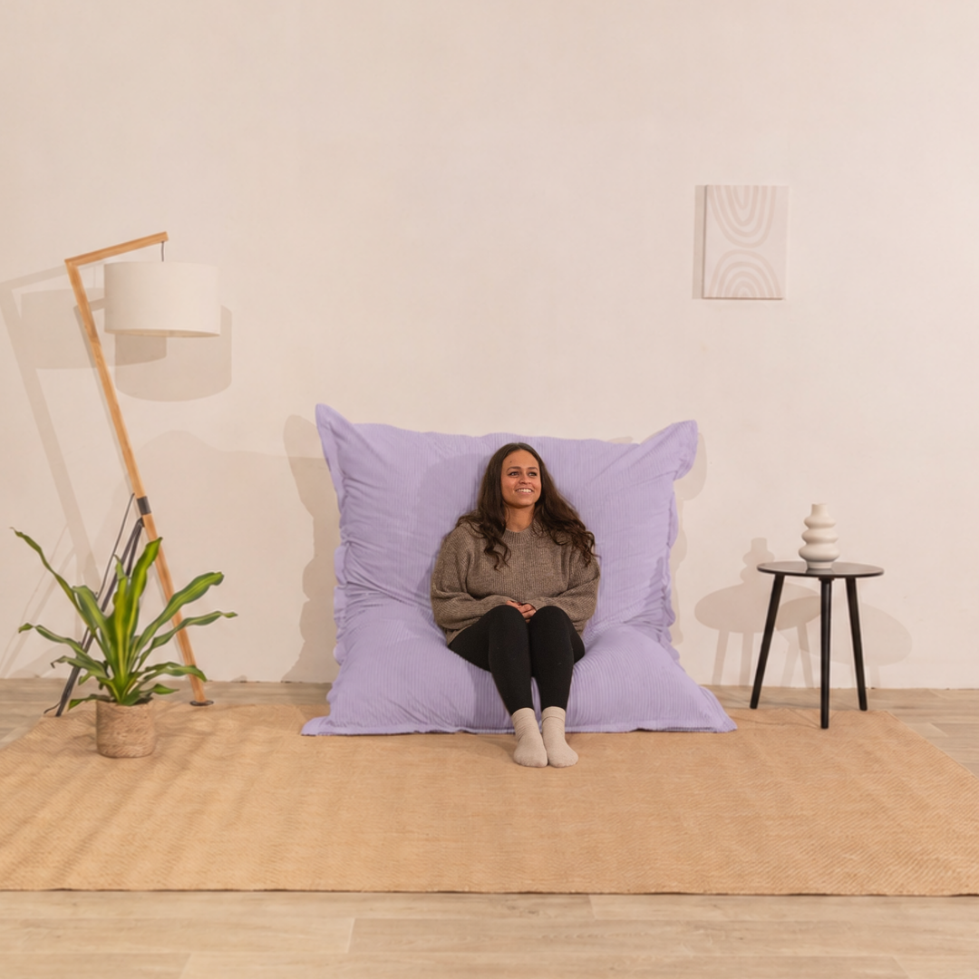 Personne assise sur un pouf 140x180 cm violet en velours côtelé, dossier appuyé contre le mur dans un décor d&