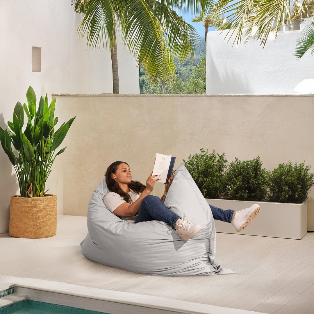 Personne allongée sur un pouf extérieur 140x180 cm au bord d’une piscine, utilisé comme assise confortable.