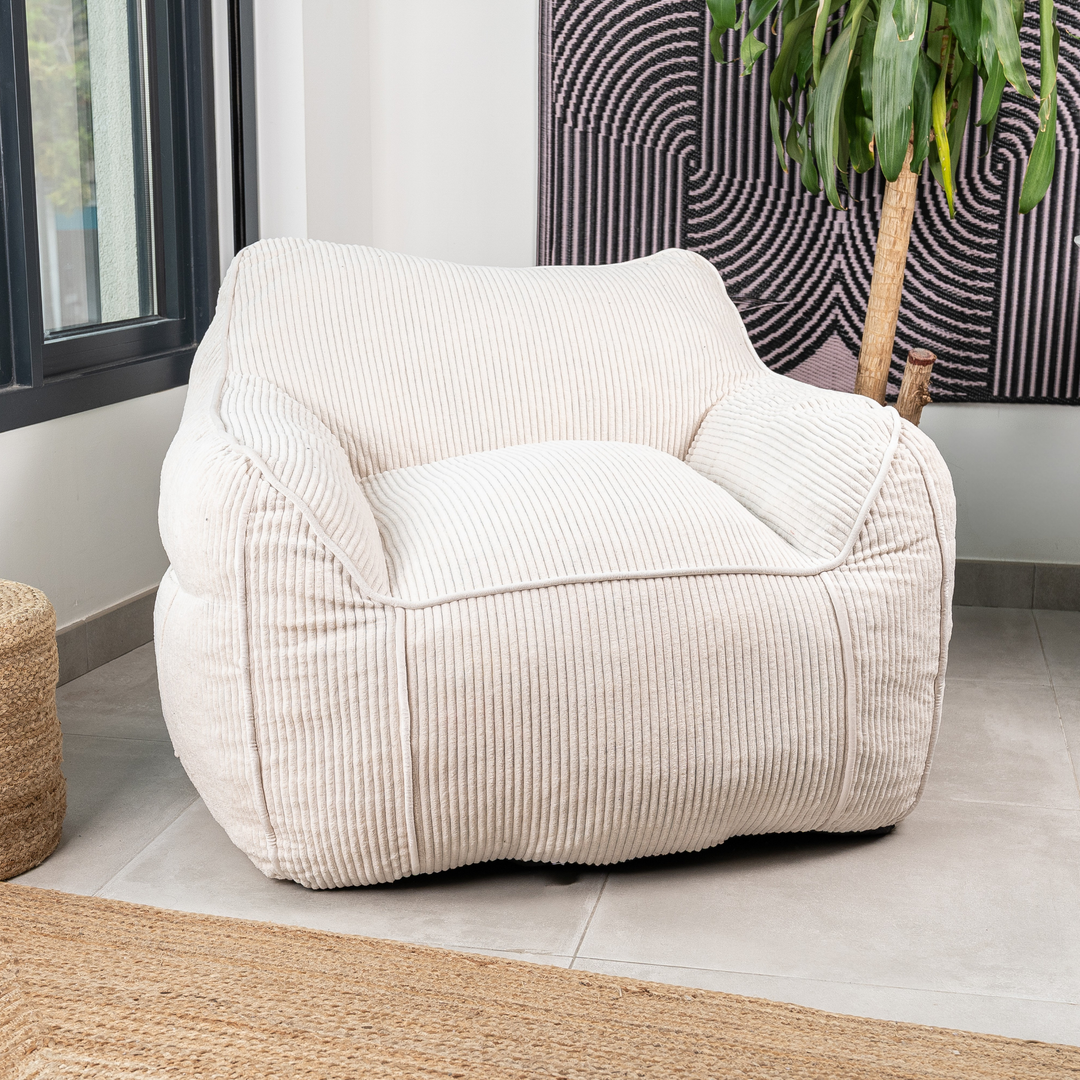 Pouf fauteuil en velours côtelé blanc cassé, assise et accoudoirs rembourrés, dans un salon