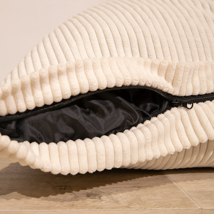 Housse amovible du pouf en velours côtelé blanc cassé, fermeture éclair visible.